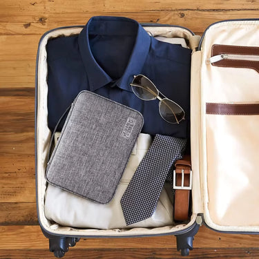 Pochette organisateur compacte pour voyage, rangée dans une valise avec chemise, cravate et lunettes, idéale pour transporter accessoires, cùbles et articles essentiels.